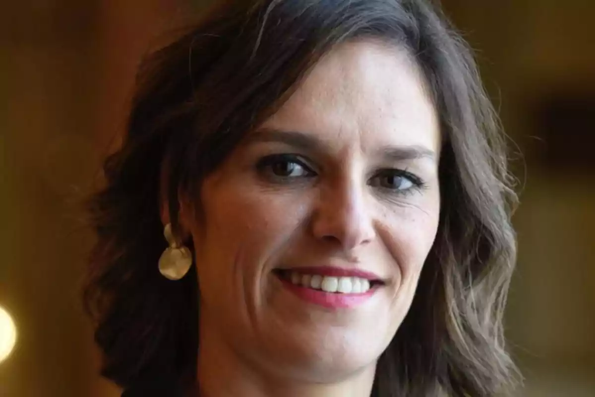 Mujer de cabello castaño corto sonriendo y usando aretes dorados en un entorno interior iluminado Mujer de cabello castaño corto sonriendo y usando aretes dorados en un entorno interior iluminado