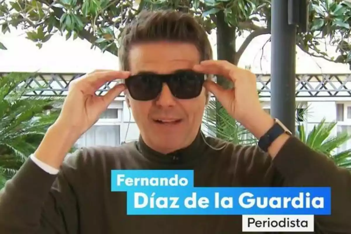 Fernando Díaz de la Guardia con gafas de sol ajustándose las monturas en un entorno exterior con plantas y estructuras metálicas al fondo.