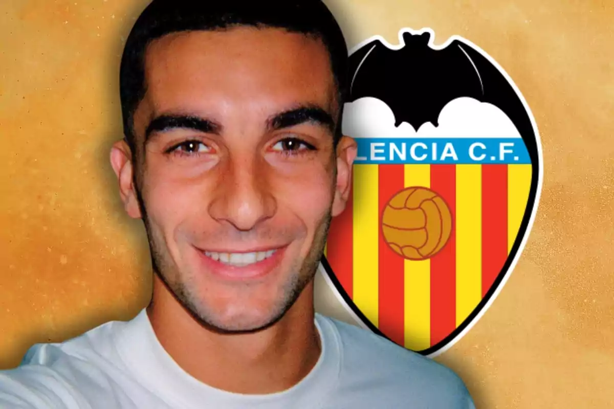 Joven sonriente con camiseta blanca frente al escudo del Valencia Club de Fútbol sobre fondo naranja