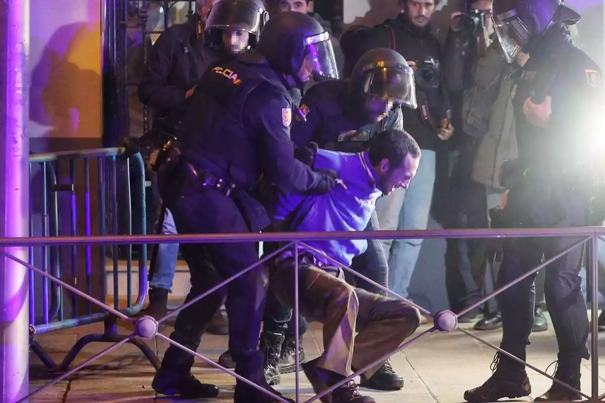 Dos agentes de Policía antidisturbios detiene un manifestante en la calle Ferraz, delante de la sede del PSOE en Madrid, mientras dos agentes más y varios periodistas miran la escena