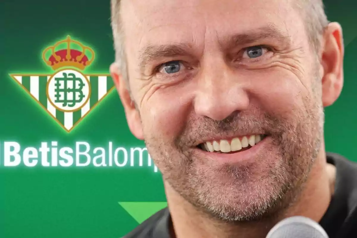 Un hombre sonriente con barba frente al logo del Real Betis Balompié.