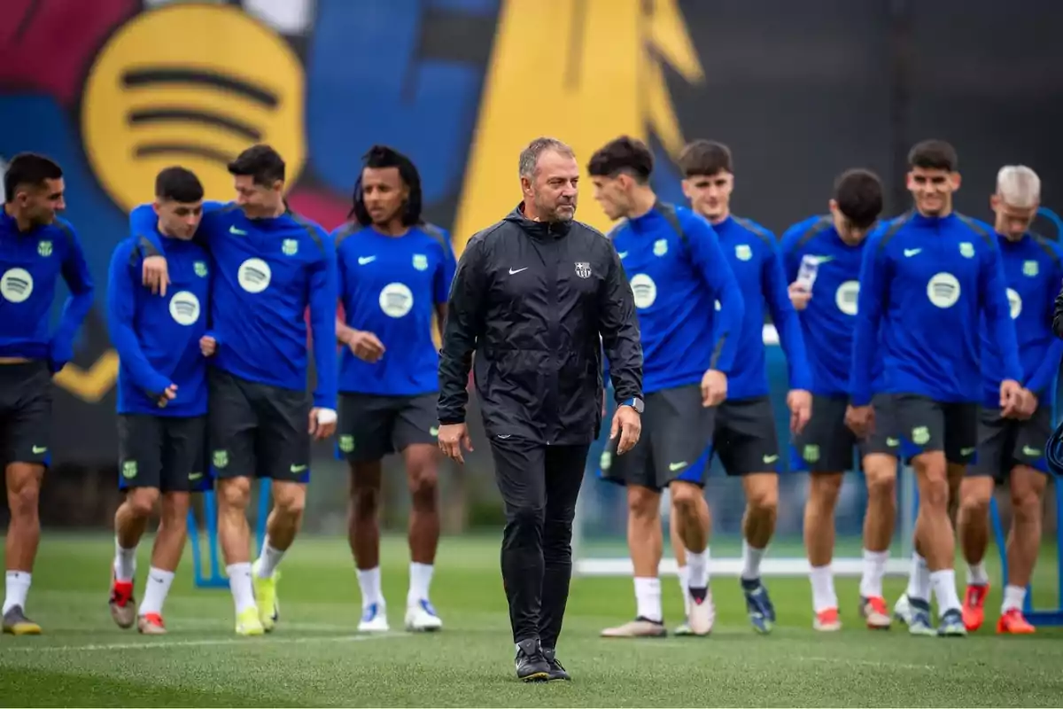 Entrenador de fútbol caminando al frente mientras jugadores del Barcelona entrenan en el campo con uniforme azul Entrenador de fútbol caminando al frente mientras jugadores del Barcelona entrenan en el campo con uniforme azul