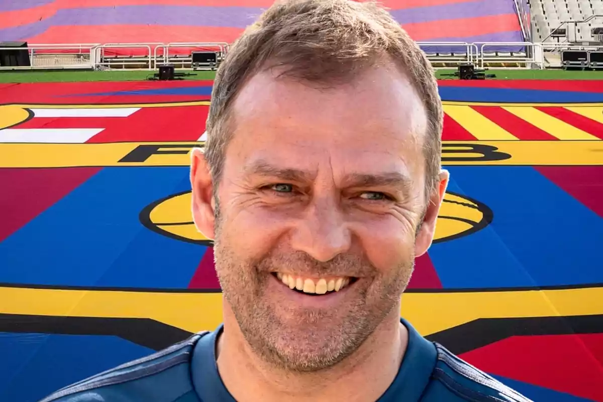 Un hombre sonriente con una camiseta azul está frente a un gran escudo del FC Barcelona en un estadio.