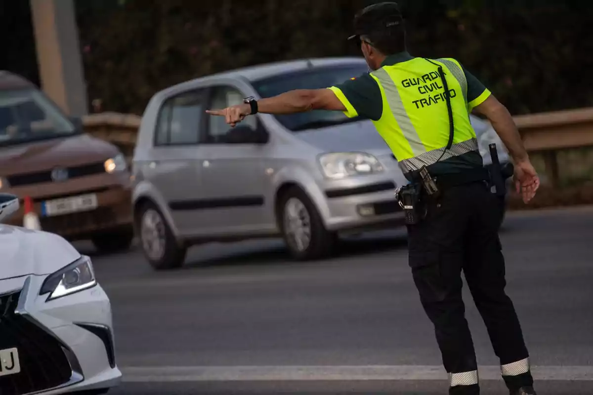 Agente de la Guardia Civil de Tráfico dirigiendo el tránsito en una carretera mientras varios coches circulan alrededor Agente de la Guardia Civil de Tráfico dirigiendo el tránsito en una carretera mientras varios coches circulan alrededor