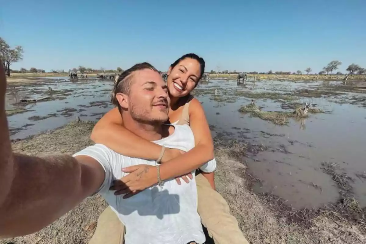 Una pareja sonriente se toma una selfie en un entorno natural con agua y vegetación.