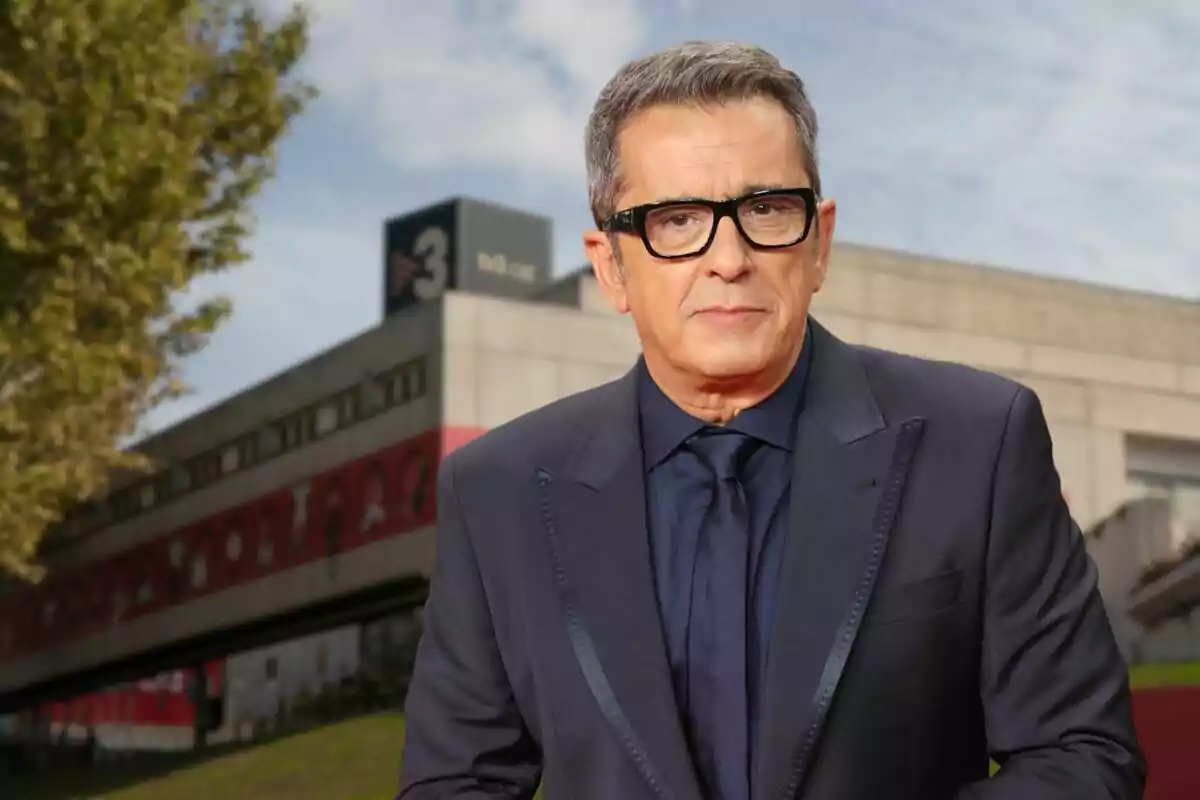 Un hombre con gafas y traje oscuro frente a un edificio con el número 3 en el fondo.