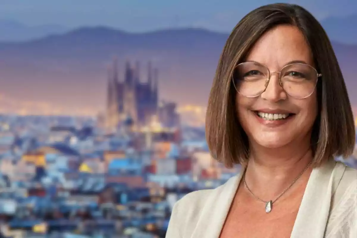 Una mujer sonriente con gafas y cabello corto frente a un fondo urbano desenfocado.