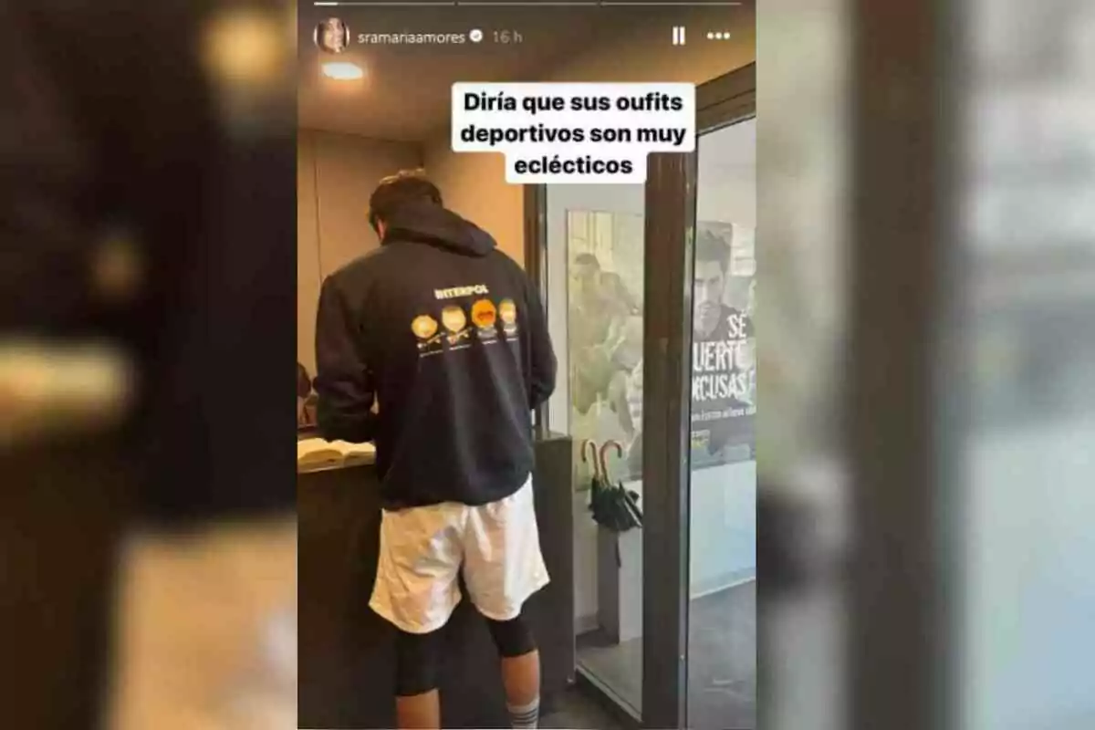 Ion Aramendi de espaldas con una sudadera negra y pantalones cortos blancos está en un interior, con un cartel en la pared y un texto superpuesto que dice Ion Aramendi de espaldas con una sudadera negra y pantalones cortos blancos está en un interior, con un cartel en la pared y un texto superpuesto que dice