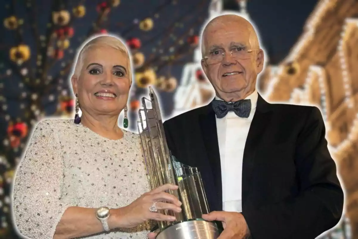 Una pareja elegantemente vestida sostiene un trofeo en un evento nocturno con luces de fondo.