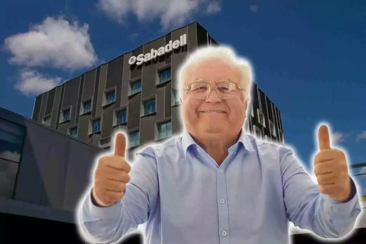 Un hombre mayor sonriente con gafas y camisa azul levanta ambos pulgares frente a un edificio con el logo de Sabadell en un día soleado.