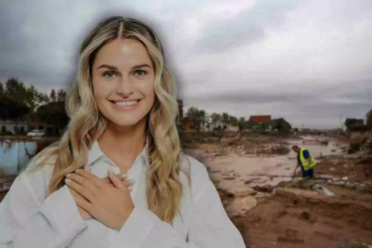 Una mujer sonriente con las manos sobre el pecho está en primer plano mientras que al fondo se observa un paisaje de escombros y una persona trabajando con un chaleco de seguridad en València.