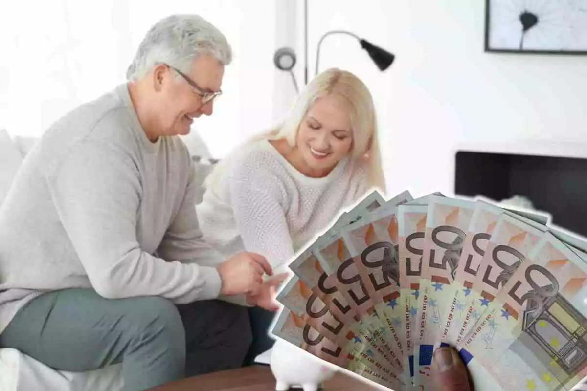 Una pareja mayor sonriente sentada en un sofá con billetes de 50 euros en primer plano.