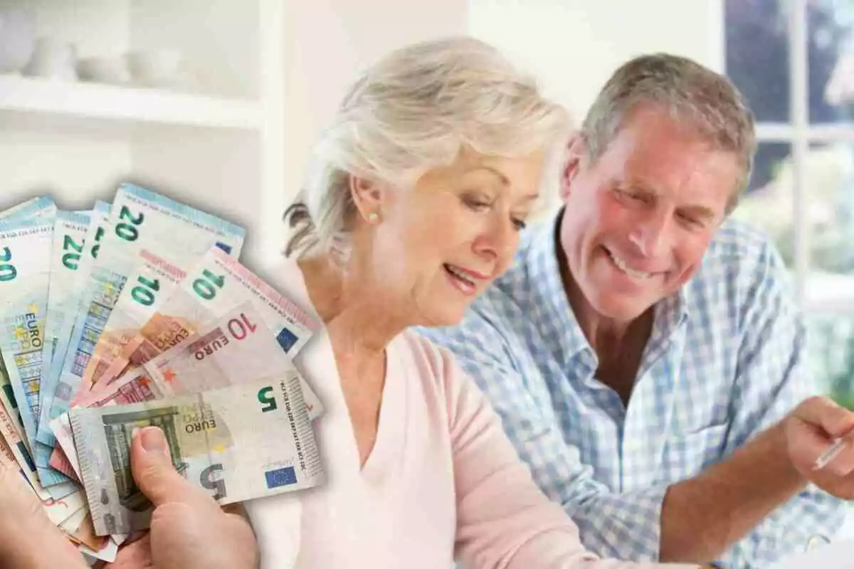 Una pareja de personas mayores sonríe mientras revisa documentos, con una mano sosteniendo varios billetes de euro en primer plano.