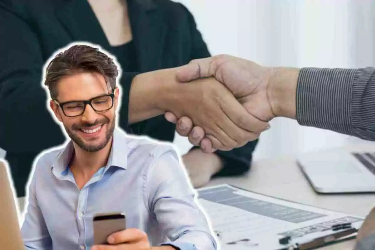 Un hombre sonriente con gafas y barba mira su teléfono móvil mientras dos personas se dan la mano en el fondo, sugiriendo un acuerdo o colaboración.