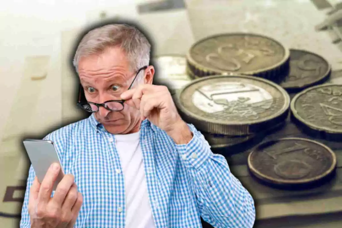 Hombre mayor con camisa a cuadros mirando sorprendido su teléfono móvil con monedas de euro en el fondo.