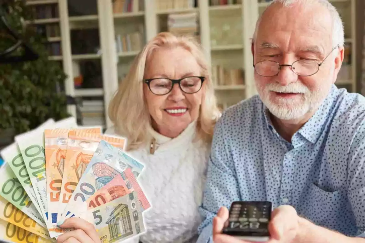 Una pareja de personas mayores sonríe mientras una de ellas sostiene varios billetes de euro y la otra un control remoto.
