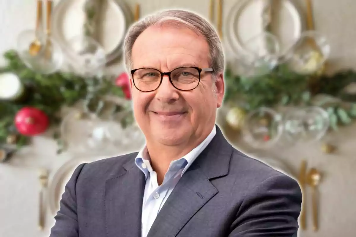 Un hombre con gafas y traje sonríe frente a un fondo decorativo con platos y vegetación.