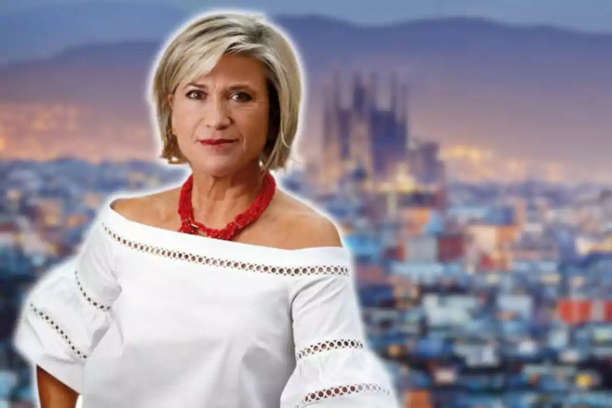 Mujer de cabello corto y canoso con blusa blanca y collar rojo posando frente a un fondo urbano desenfocado.