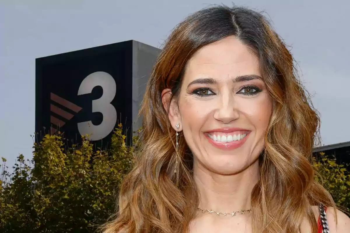 Mujer sonriendo frente a un edificio con el logo de un canal de televisión.