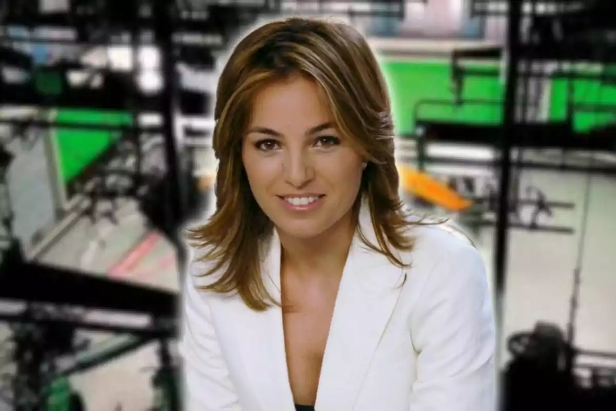 Mujer con chaqueta blanca sonriendo frente a un fondo borroso de estudio.