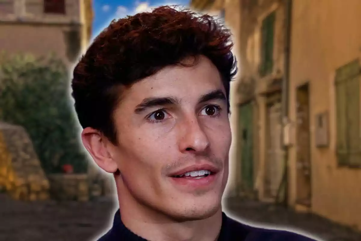 Un hombre de cabello oscuro y expresión atenta está en primer plano con un fondo de calle empedrada y edificios antiguos.