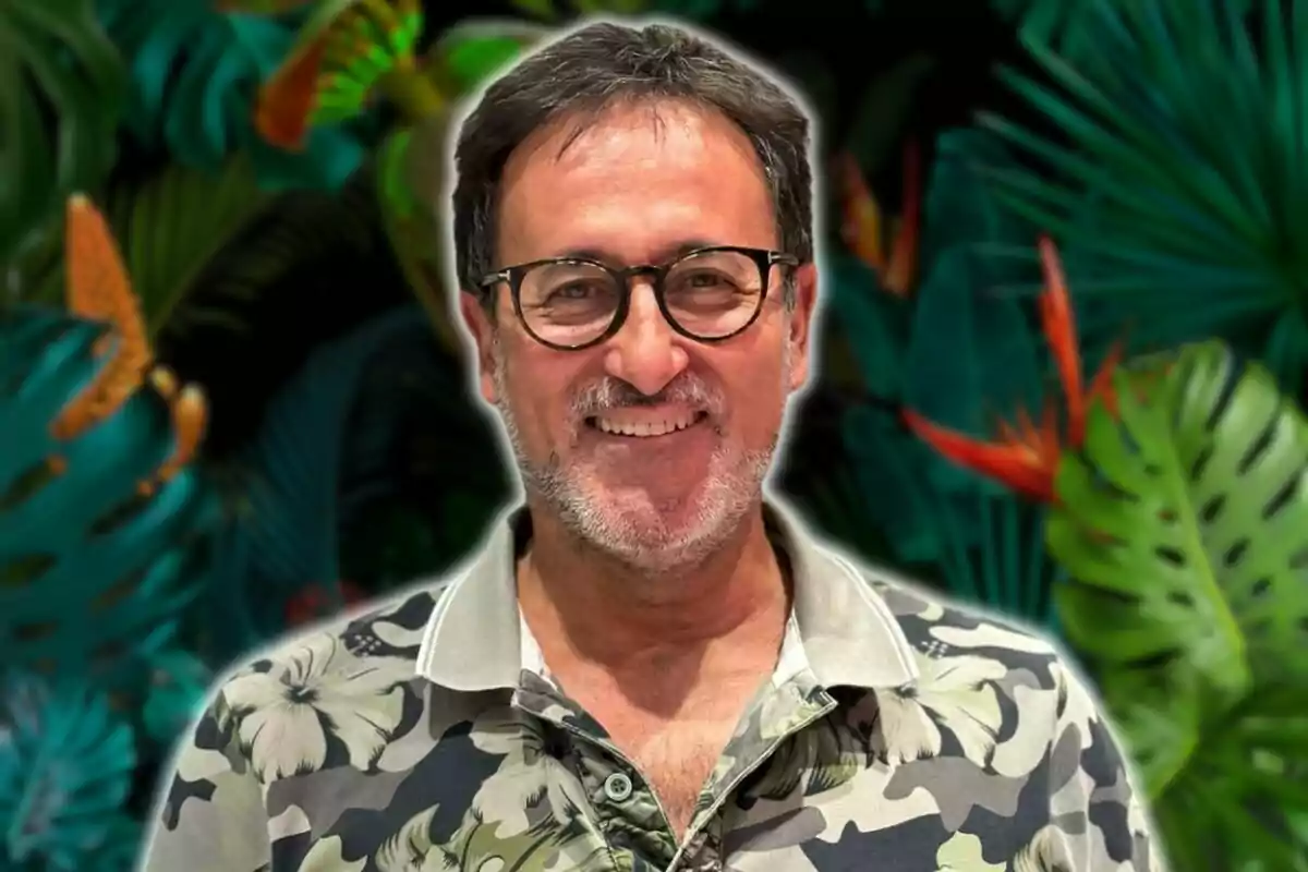 Un hombre con gafas y barba sonríe frente a un fondo de hojas tropicales.