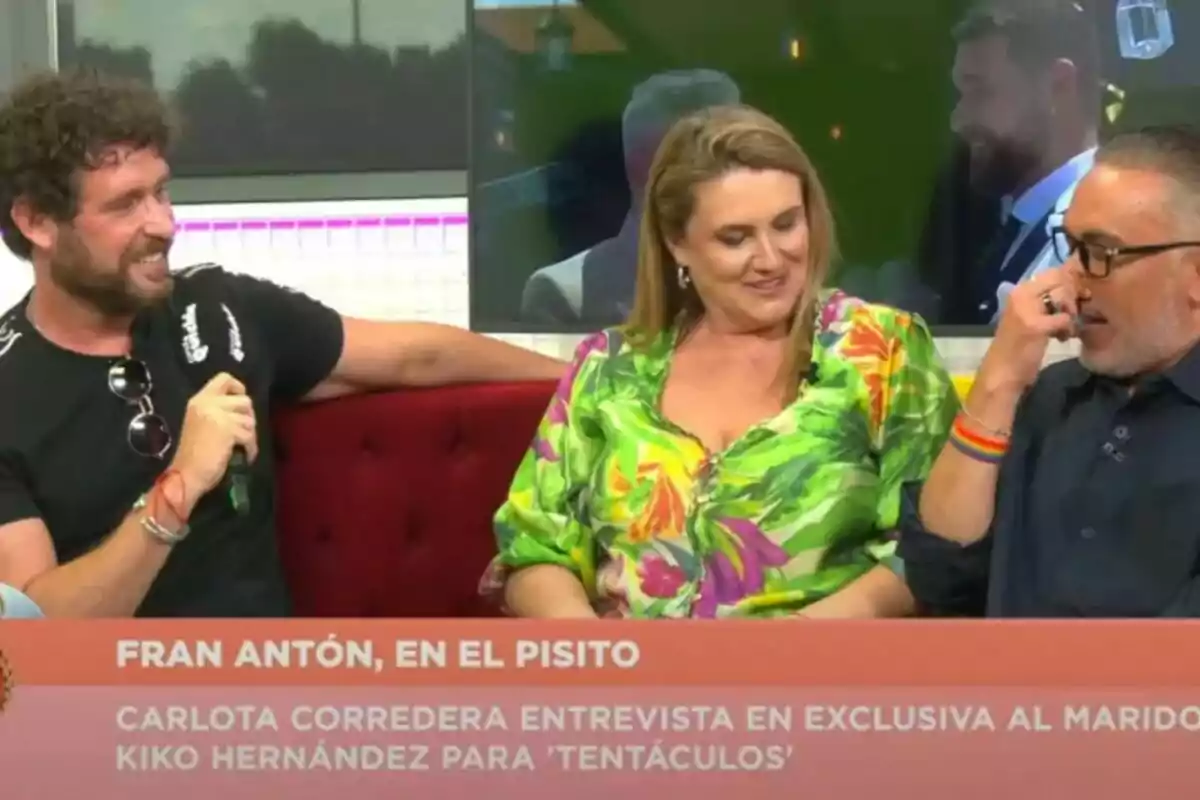 Fran Antón, Carlota Corredera y Kiko Hernández sentadas en un sofá rojo conversan y sonríen durante una entrevista en Tentáculos, con un rótulo informativo en la parte inferior de la imagen.