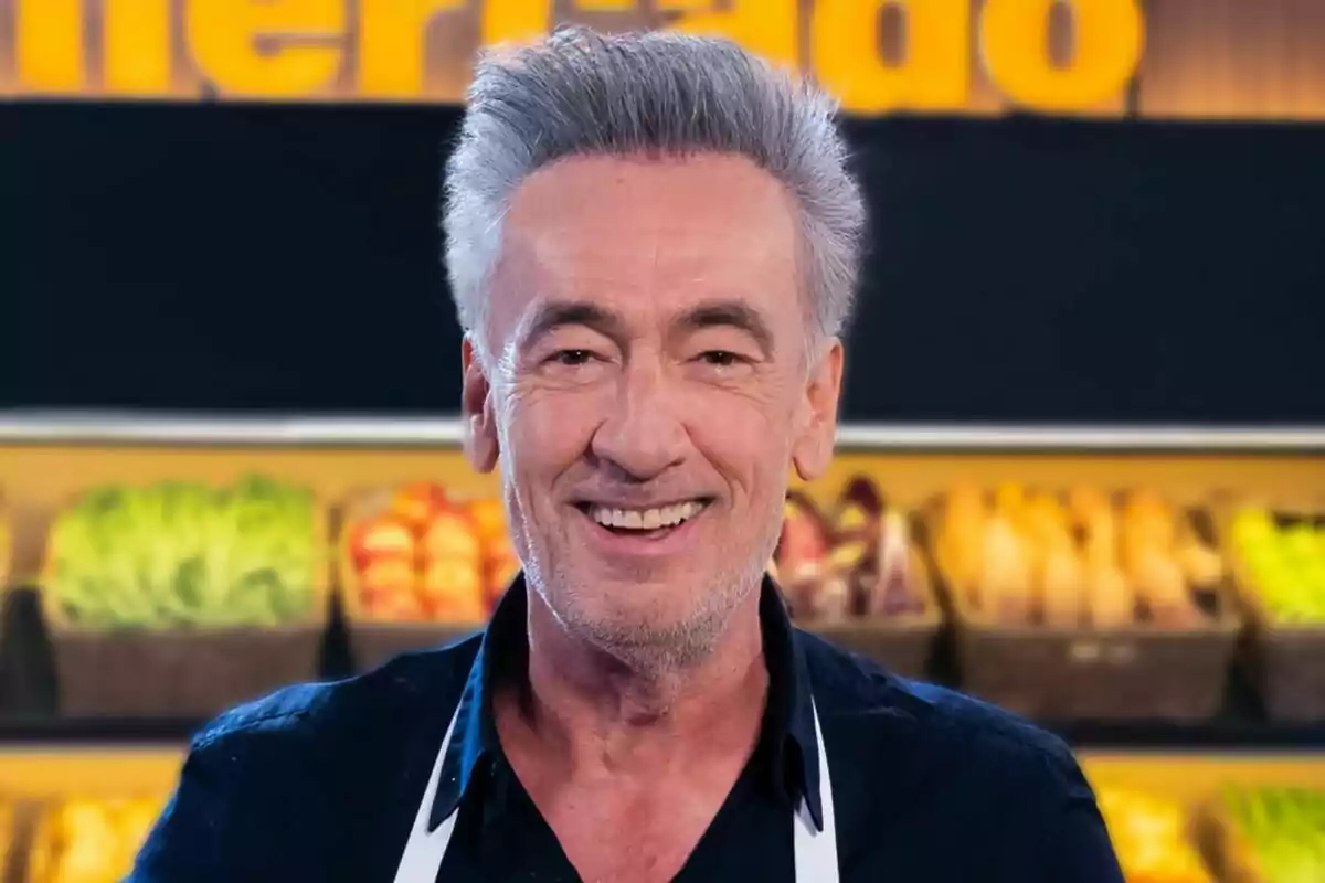 Francis Lorenzo de cabello canoso sonriendo con fondo de frutas y verduras en MasterChef Celebrity.