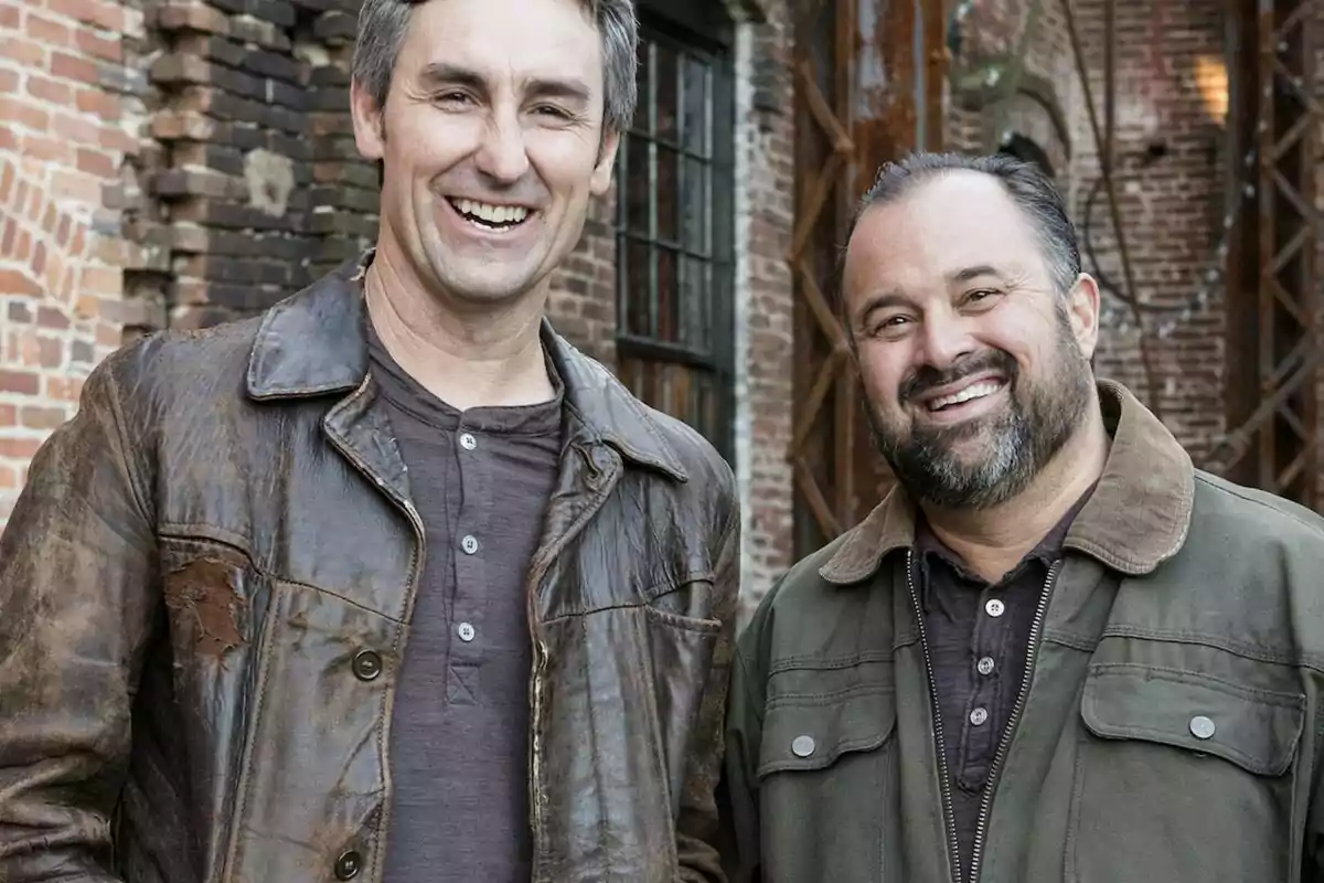 Frank Fritz y Mike Wolfe sonrientes posan frente a un edificio de ladrillos.