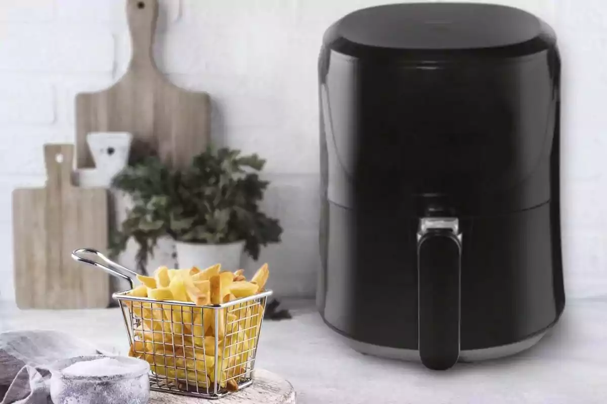 Una freidora de aire negra junto a una canasta de papas fritas sobre una mesa, con tablas de cortar y plantas en el fondo. Una freidora de aire negra junto a una canasta de papas fritas sobre una mesa, con tablas de cortar y plantas en el fondo.