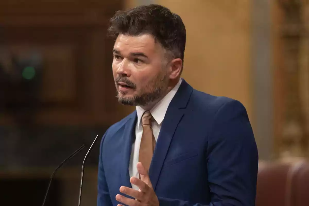 Hombre con traje azul y corbata marrón hablando en un podio.