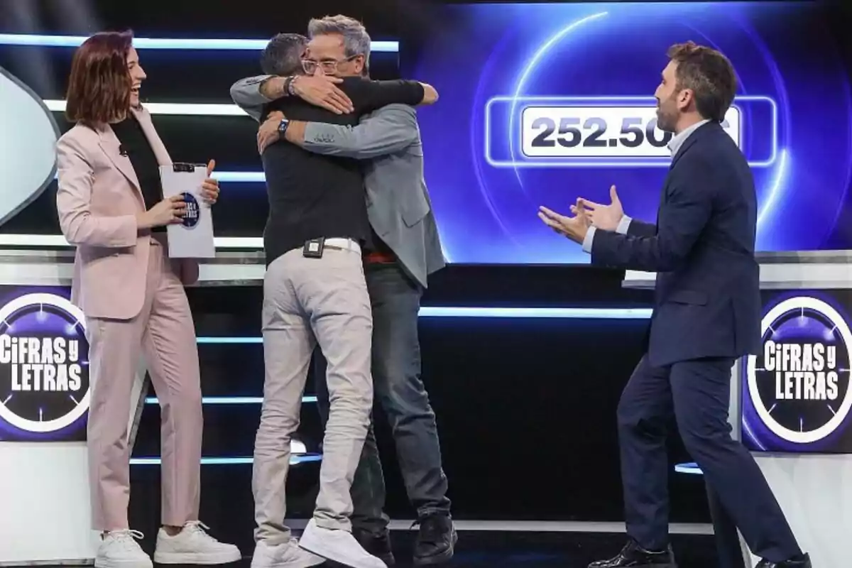 Cuatro personas como Aitor Albizua celebran en un set de televisión del programa Cifras y Letras mientras dos de ellas se abrazan y una pantalla muestra el número 252.500