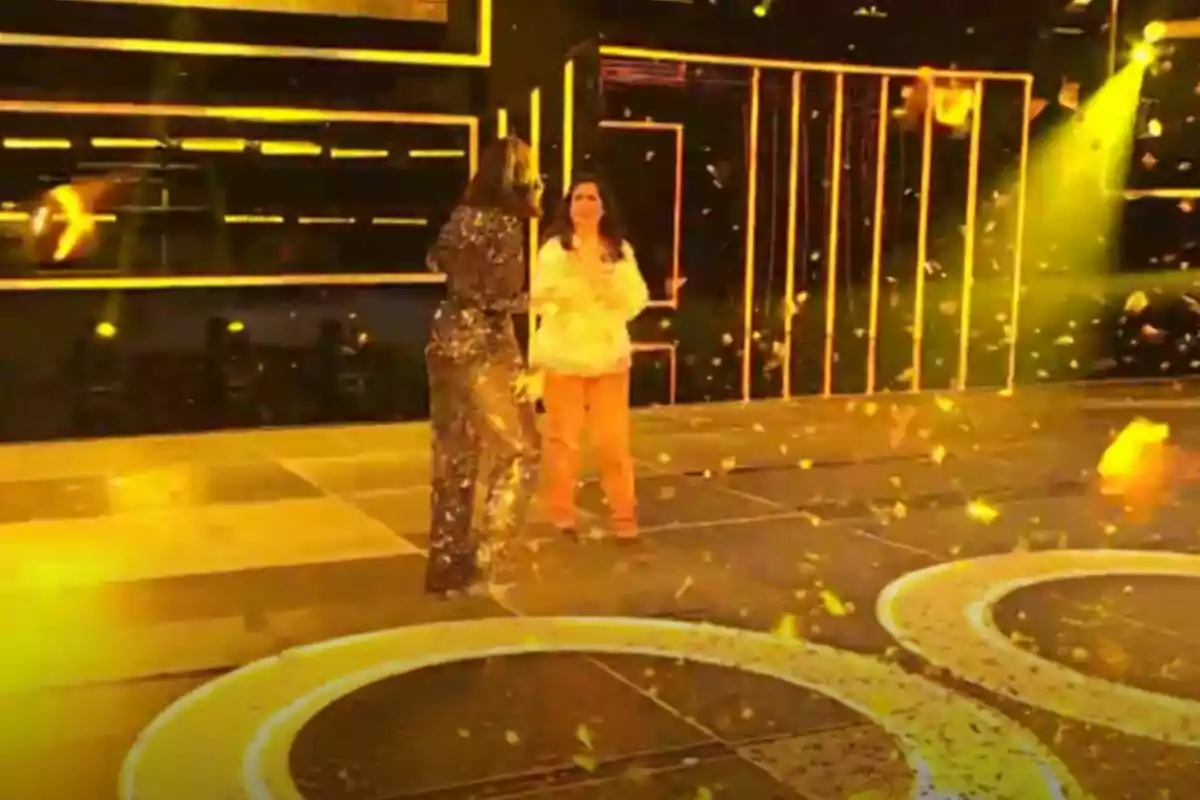 Mercedes y Chenoa en un escenario iluminado con luces amarillas y confeti dorado cayendo alrededor en The Floor. Mercedes y Chenoa en un escenario iluminado con luces amarillas y confeti dorado cayendo alrededor en The Floor.