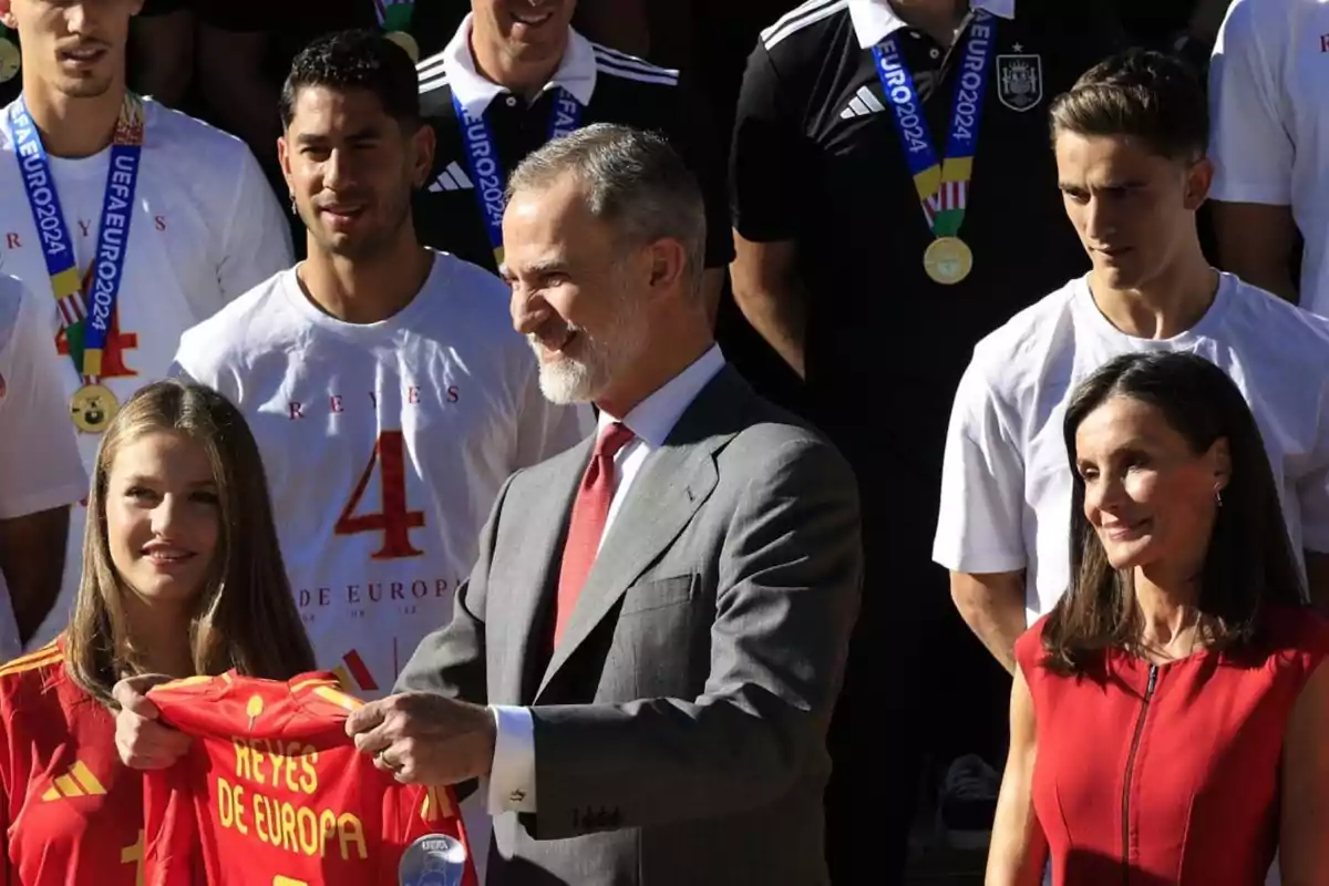 Un grupo de personas, algunas con medallas, posan para una foto; una persona sostiene una camiseta roja que dice 