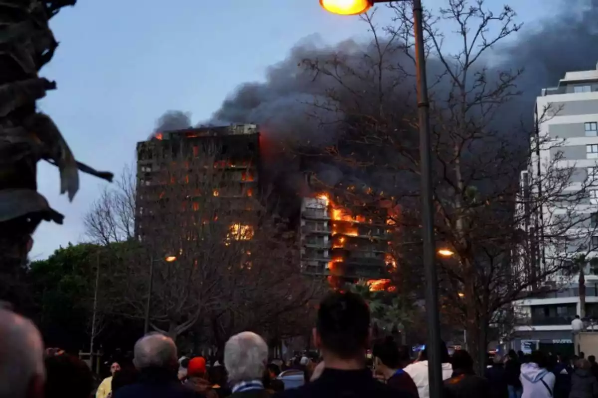 Gente presenciando el incendio del edificio de Valencia con llamas saliendo por los balcones