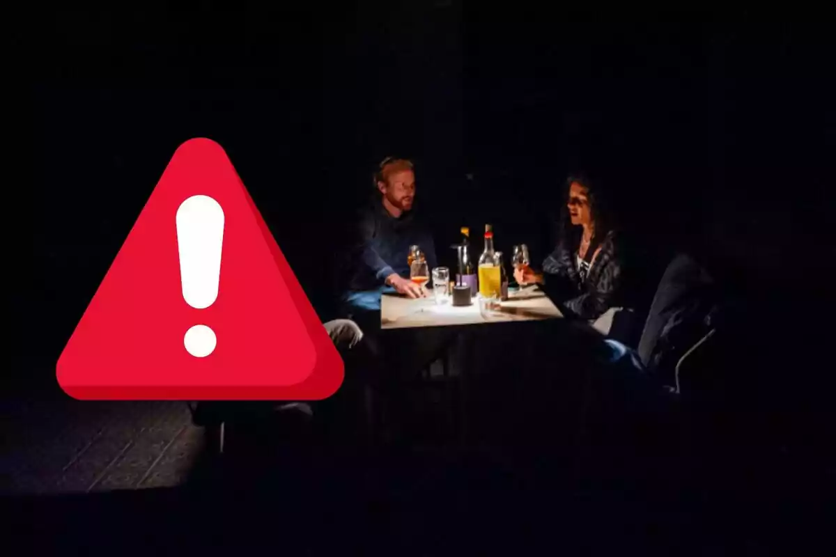 Una pareja sentada en una mesa con bebidas en un ambiente oscuro y un ícono de advertencia superpuesto. Una pareja sentada en una mesa con bebidas en un ambiente oscuro y un ícono de advertencia superpuesto.