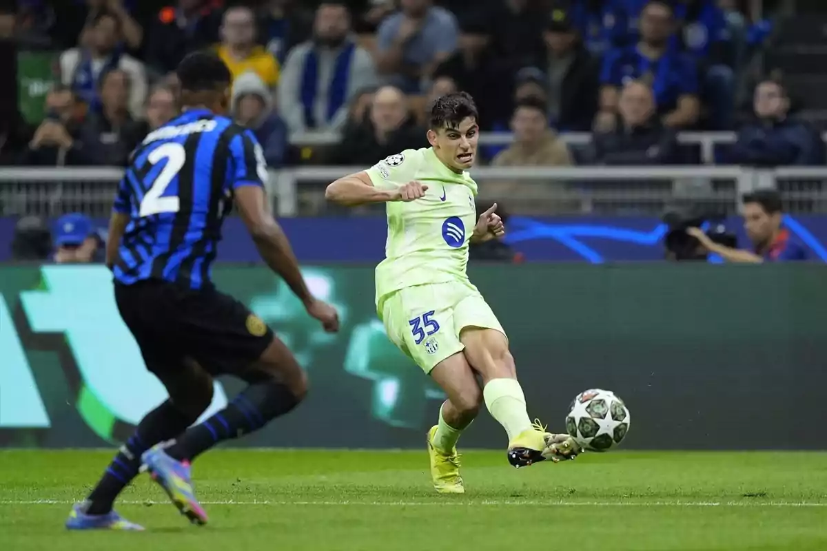 Un jugador de fútbol con uniforme claro controla el balón mientras un oponente con uniforme a rayas negras y azules se aproxima en un estadio lleno de espectadores. Un jugador de fútbol con uniforme claro controla el balón mientras un oponente con uniforme a rayas negras y azules se aproxima en un estadio lleno de espectadores.