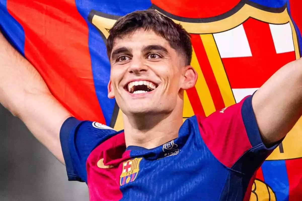 Un jugador de fútbol sonríe mientras sostiene una bandera del FC Barcelona.