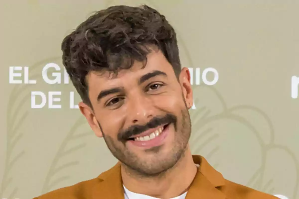 Germán González con barba y bigote sonriendo frente a un fondo verde con texto en la presentación de El Gran Premio de la Cocina.