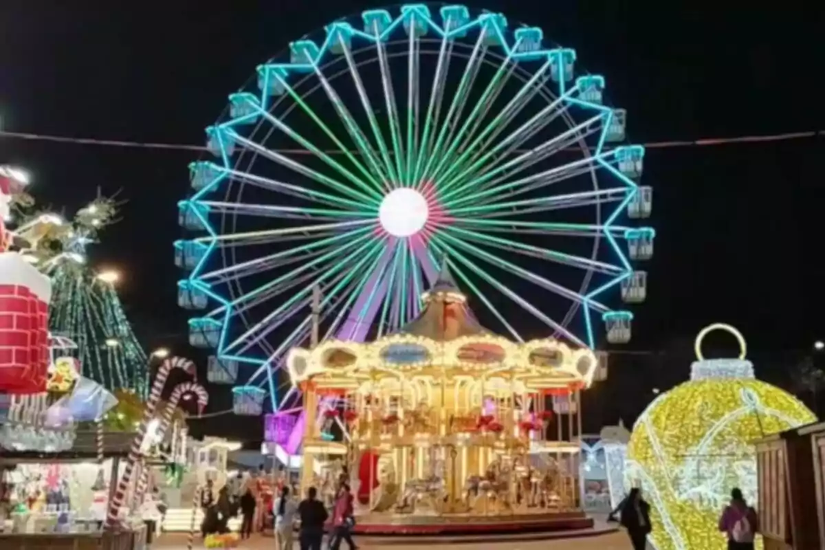 Una noria iluminada con luces de colores en un parque de atracciones nocturno con un carrusel y decoraciones festivas.