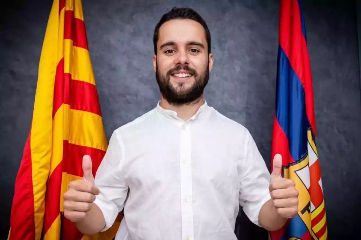 Jonatan Giráldez posa con los pulgares hacia arriba delante de una bandera del FC Barcelona