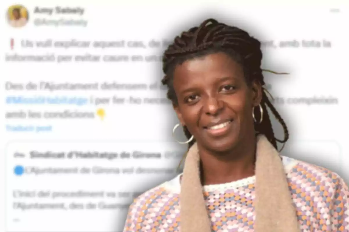Mujer de cabello trenzado y suéter claro sonriendo frente a un fondo borroso con texto en catalán.