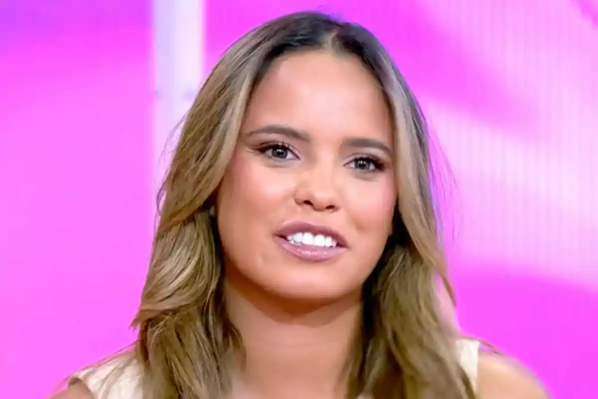 Gloria Camila con cabello largo y suelto sonriendo frente a un fondo rosa en 'Tardear'.