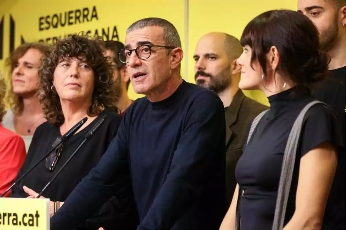 Un grupo de personas en una conferencia de prensa frente a un fondo amarillo con el logotipo de un partido político.