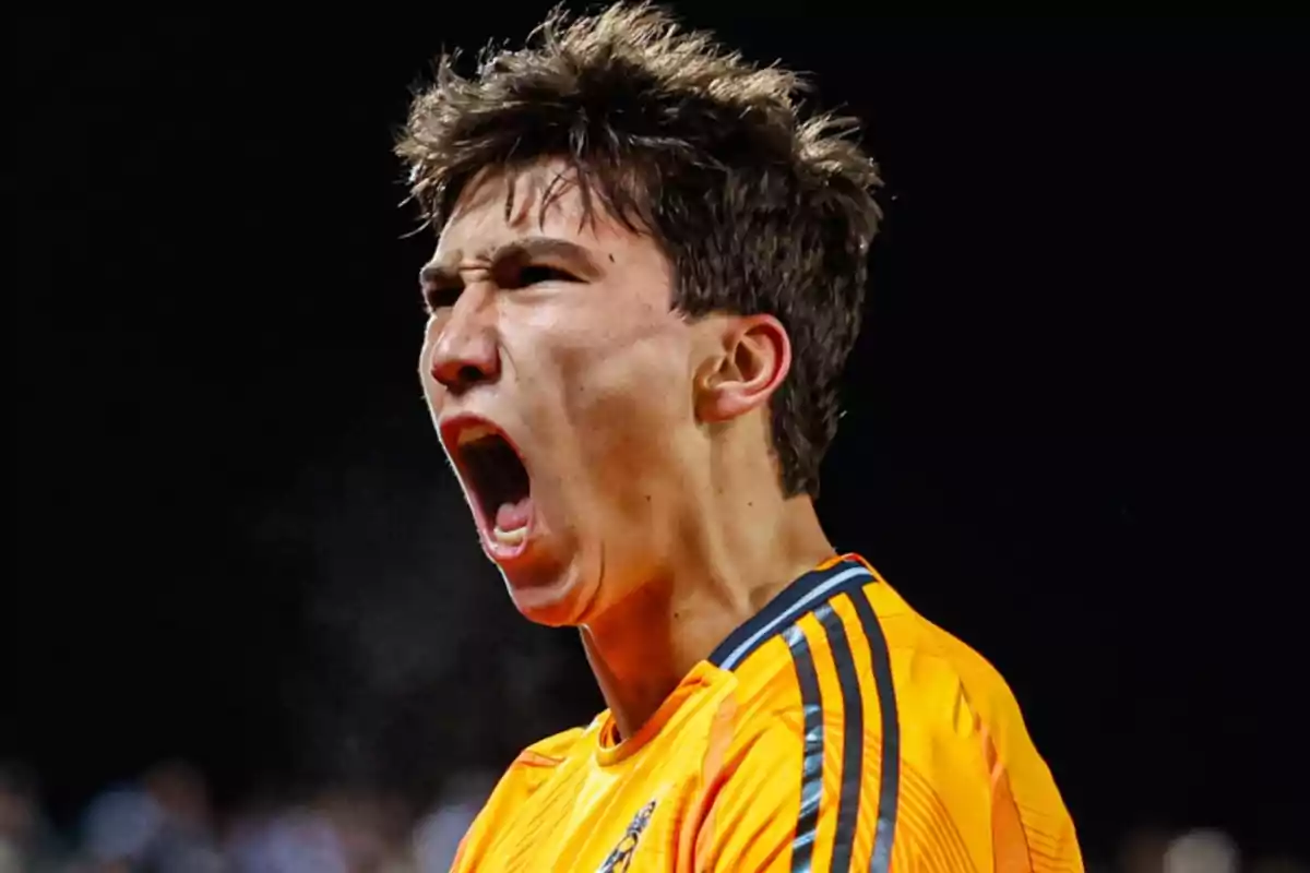 Joven con uniforme deportivo naranja grita con expresión de euforia durante un evento nocturno Joven con uniforme deportivo naranja grita con expresión de euforia durante un evento nocturno