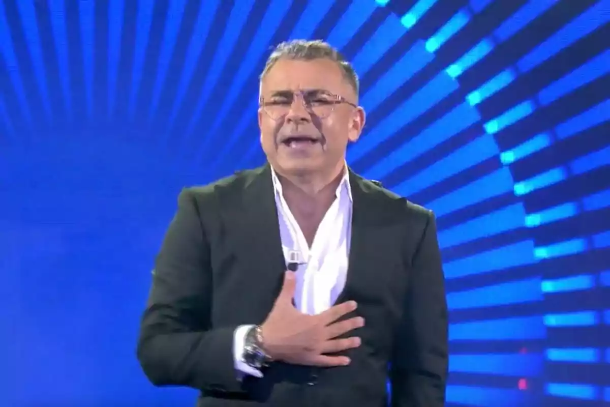 Jorge Javier Vázquez con gafas y traje oscuro hablando en un escenario con fondo azul y rayos de luz. Captura de 'Gran Hermano' el 5 de septiembre de 2024