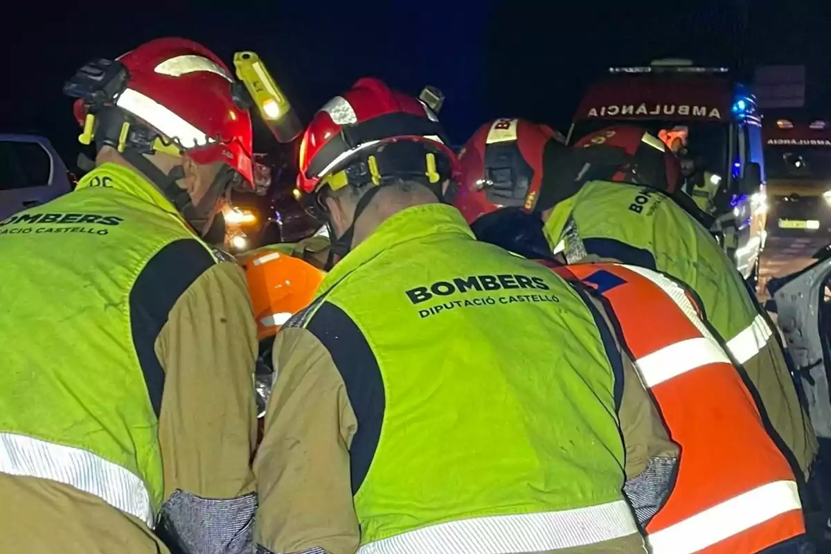 Bomberos con cascos rojos y chalecos reflectantes trabajan en un operativo nocturno junto a una ambulancia. Bomberos con cascos rojos y chalecos reflectantes trabajan en un operativo nocturno junto a una ambulancia.