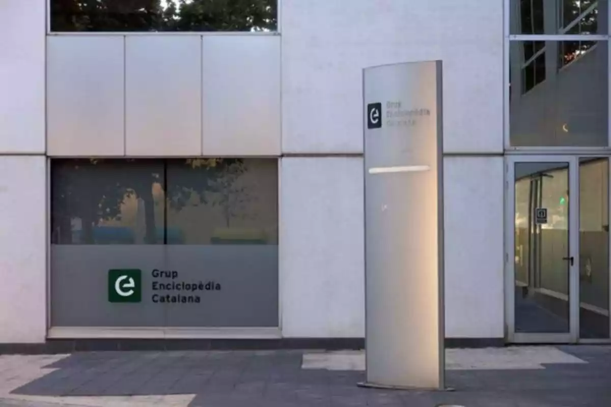 Imagen del exterior de las oficinas de Grup Enciclopedia con una columna gris alta con el nombre de la marca Imagen del exterior de las oficinas de Grup Enciclopedia con una columna gris alta con el nombre de la marca