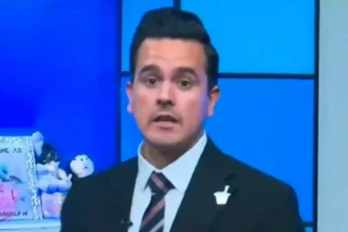 Gustavo Macalpín con traje y corbata aparece en un estudio de televisión con fondo azul.