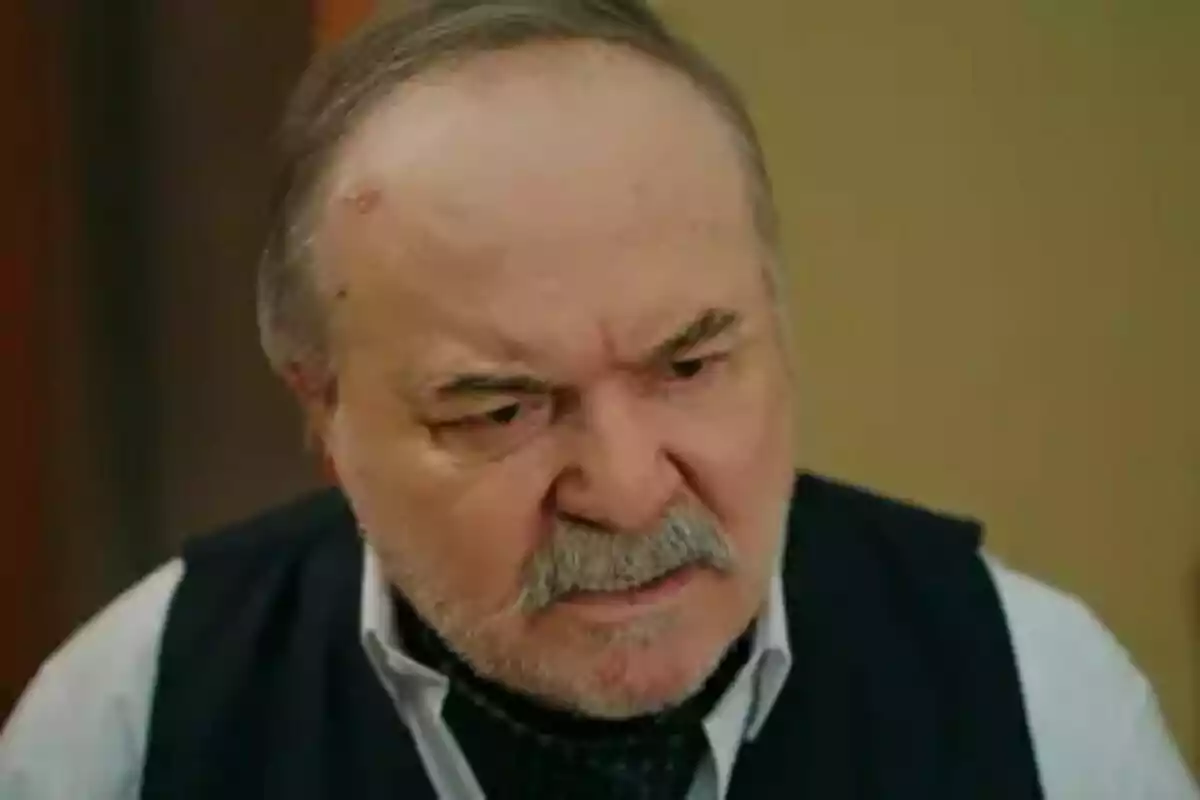Halis mayor con expresión seria y bigote, vistiendo camisa y chaleco oscuro en Una nueva vida. Halis mayor con expresión seria y bigote, vistiendo camisa y chaleco oscuro en Una nueva vida.